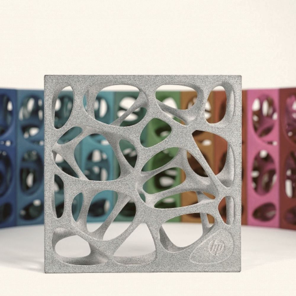 A 3D-printed gray object with an organic pattern takes center stage, surrounded by a vibrant array of similar, 3D dyeing-enhanced pieces in various colors.